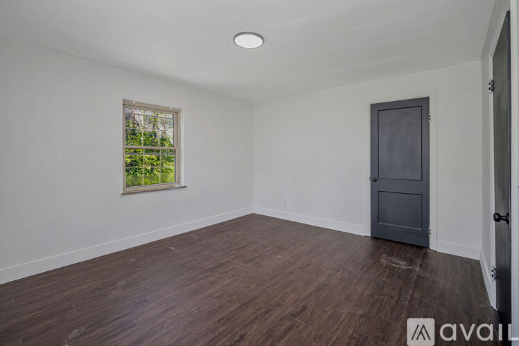 A room with wooden flooring and a window with a view of trees.