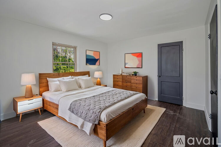 A bedroom with a large bed, a nightstand with a lamp, and a painting on the wall.