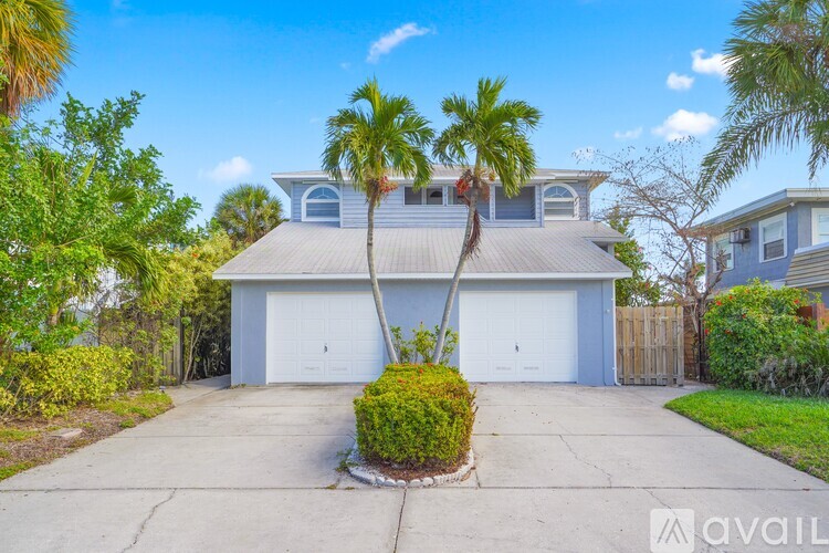 A house with a driveway and two palm trees in front.
