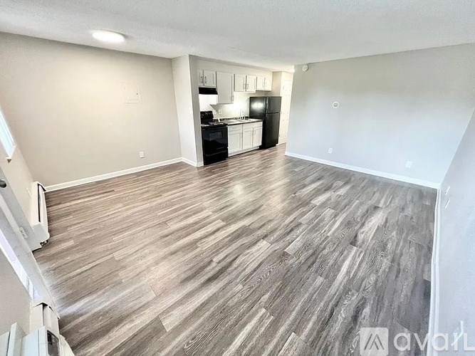 A spacious living room with wood flooring and a kitchen in the background.
