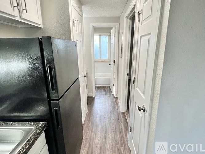 A narrow hallway with a black fridge and white cabinets.