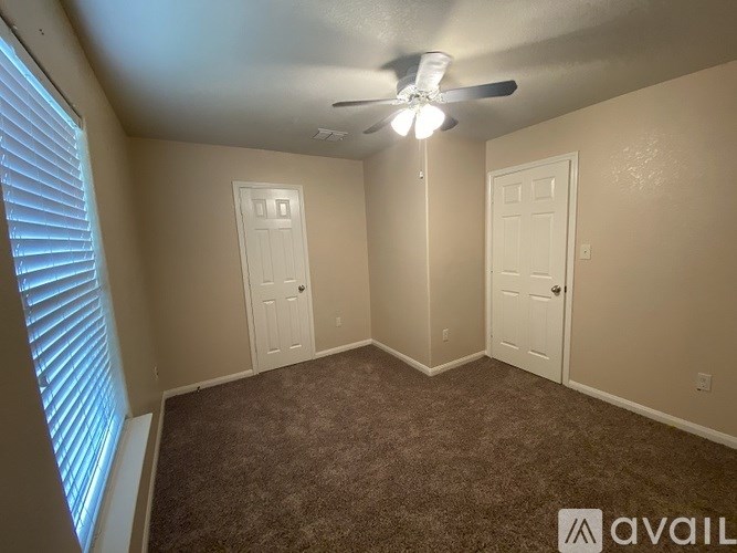 A room with a carpeted floor, two doors, and a ceiling fan.