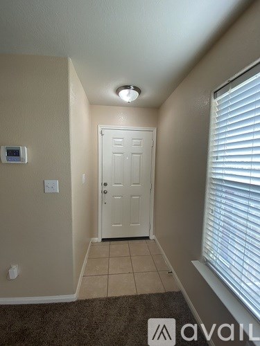 A hallway with a door, a window with blinds, and a light on the ceiling.