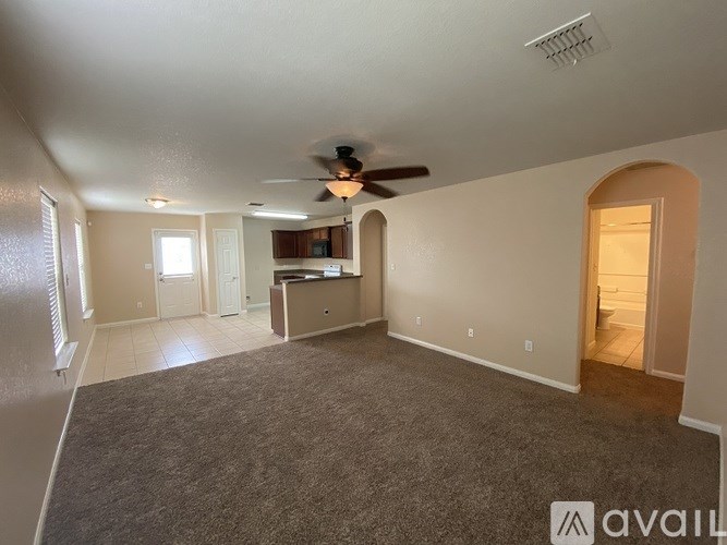 A spacious living room with a ceiling fan and a kitchenette in the background.