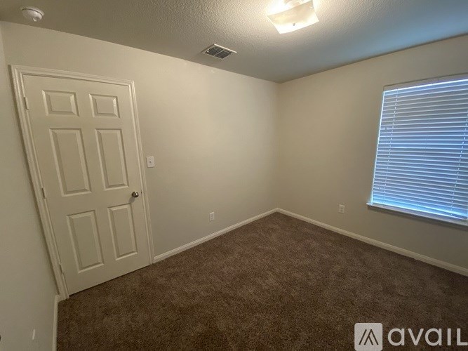 A room with a carpeted floor, a door, and a window with blinds.