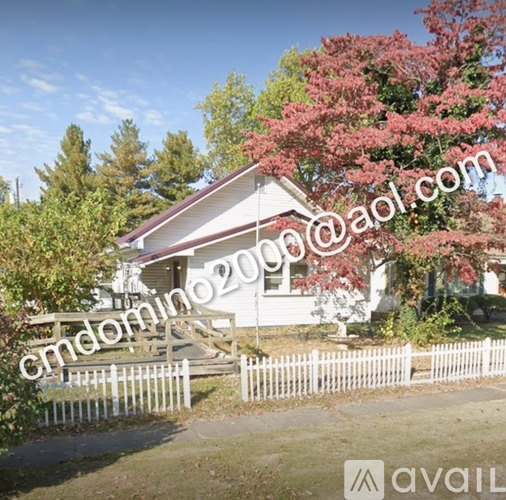 A house with a white picket fence and a tree with pink flowers in front.
