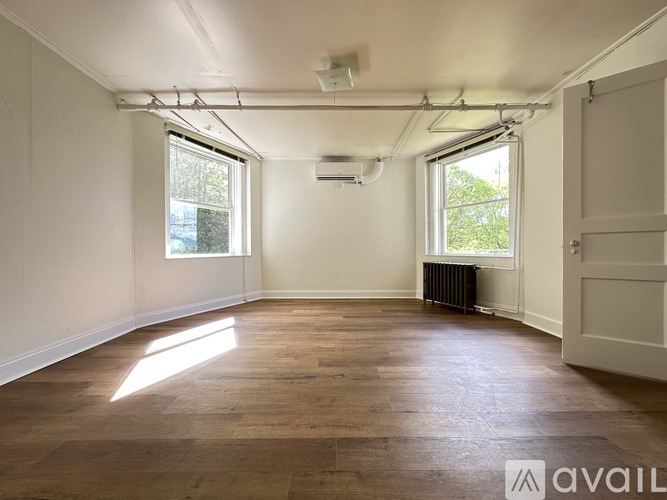 A room with wooden flooring and white walls, with a window on the left and a door on the right.