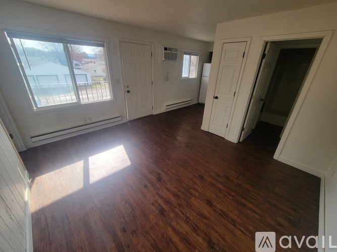 A room with wooden floors and white walls, with a window on the left side.