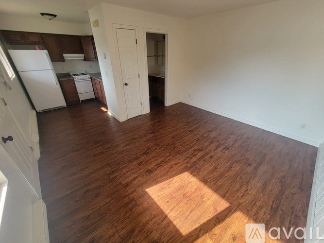 A room with wooden flooring and a kitchen area in the background.