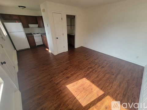 A room with wooden flooring and a kitchen area in the background.