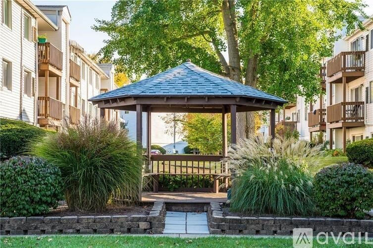 A gazebo is surrounded by a small garden and apartment buildings.