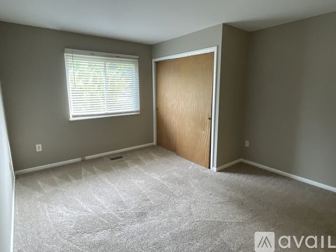 A room with a carpeted floor, a window with blinds, and a wooden door.