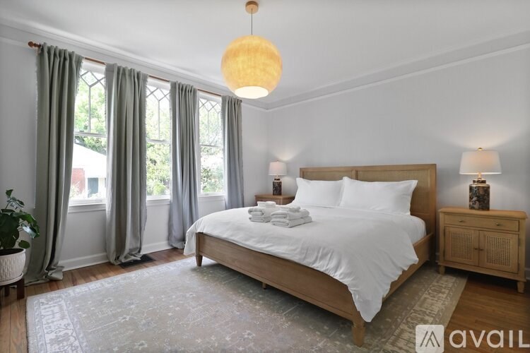 A bedroom with a large bed, a nightstand, and a window with curtains.