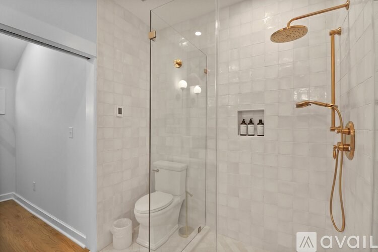 A bathroom with a toilet, a glass shower stall, and a gold shower head.