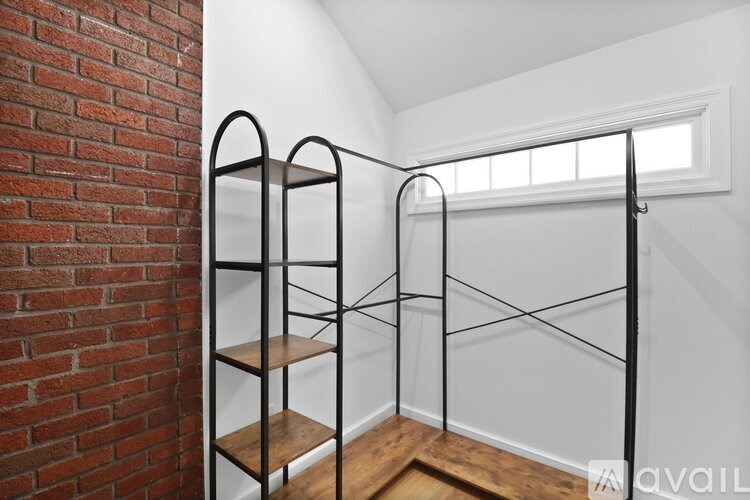 A shelving unit with four shelves is in a room with a brick wall and a window.