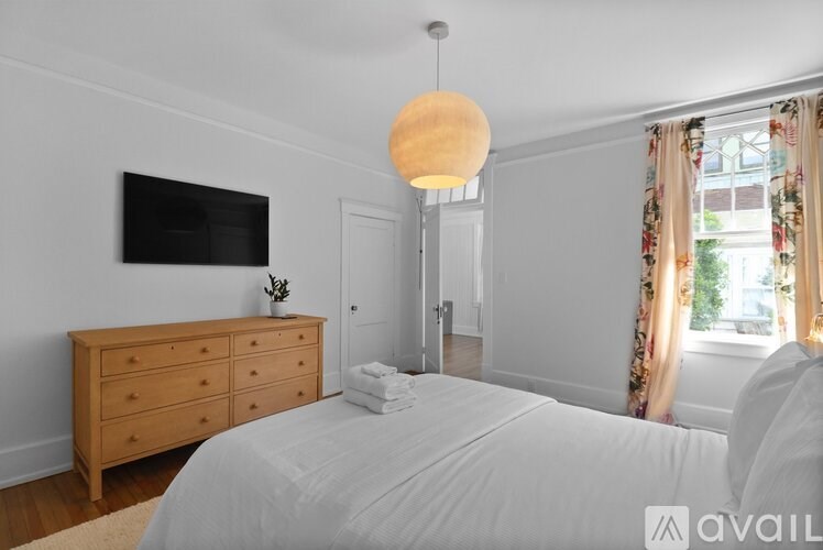 A bedroom with a large bed, a wooden dresser, and a flat-screen TV mounted on the wall.