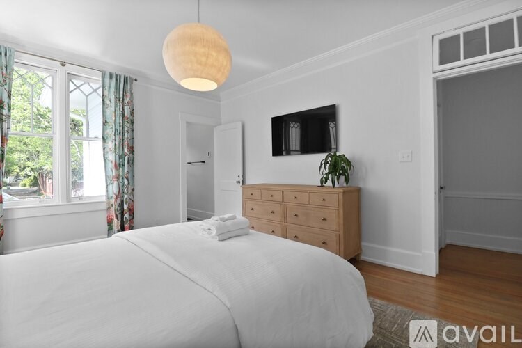 A bedroom with a large bed, a wooden dresser, and a window with curtains.