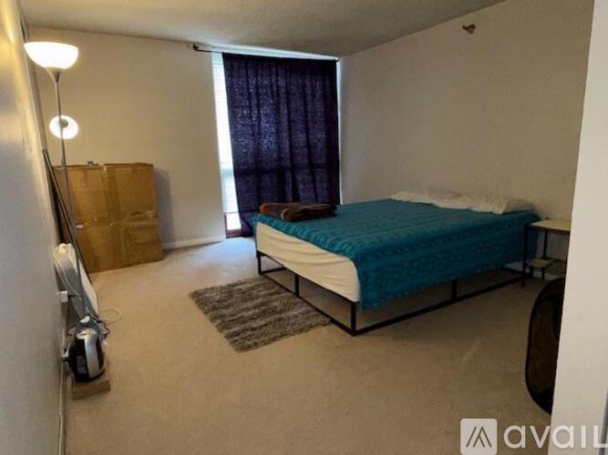 A bedroom with a bed, a rug, a fan, and a window with curtains.