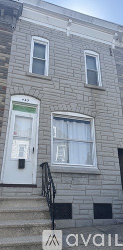 A grey house with a white door and a window with white curtains.
