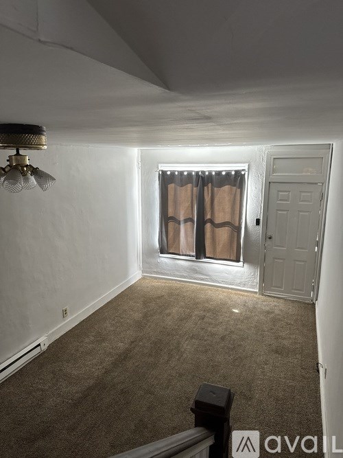A room with a carpeted floor, a door, and a window with curtains.