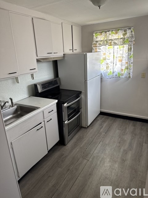 A kitchen with white cabinets and a window with a floral curtain.
