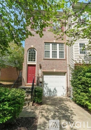 A house with a red door and a white garage door is surrounded by greenery.
