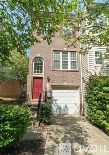 A house with a red door and a white garage door is surrounded by greenery.
