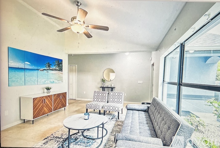 A living room with a grey sofa, a coffee table, and a painting of a beach scene on the wall.