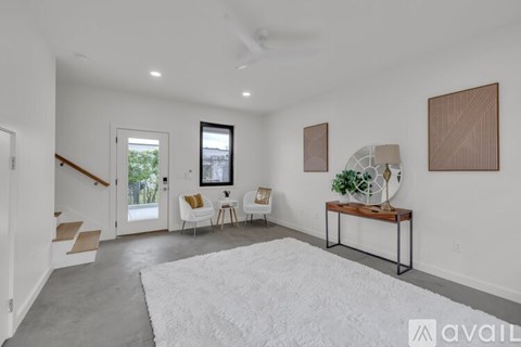 A spacious living room with a white rug, a wooden table, and a ceiling fan.