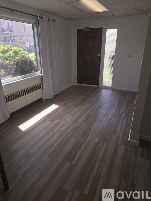 A room with wooden flooring and a window with white curtains.