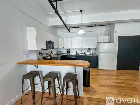 A kitchen with white cabinets and a wooden island with three stools.