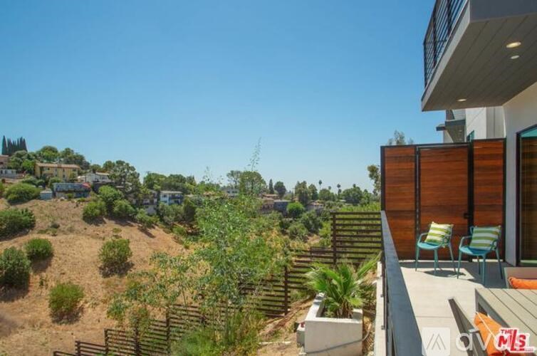A house with a patio and a view of a hill with trees and shrubs.