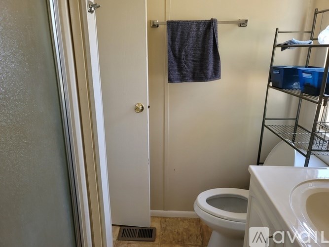 A bathroom with a toilet, a towel hanging on the door, and a shelf with storage boxes.