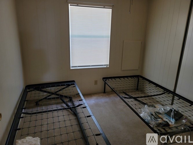 A room with a bed frame and a window with blinds.