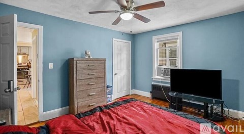 A room with a ceiling fan and a red bedspread.