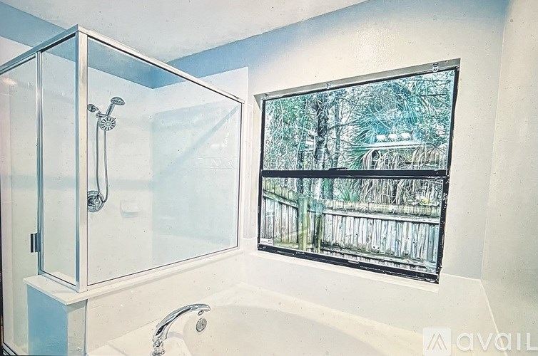 A bathroom with a glass shower enclosure and a window with a view of a wooden fence.