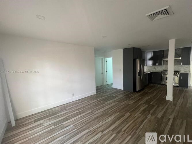 A room with wooden flooring and a kitchen area in the background.