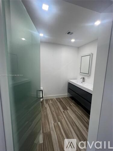 A bathroom with a glass shower door and wooden flooring.