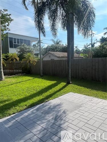A backyard with a paved area, a fence, and a palm tree.