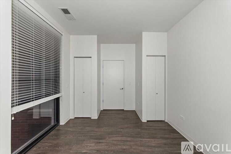 A room with white walls and a window with blinds on the left side.