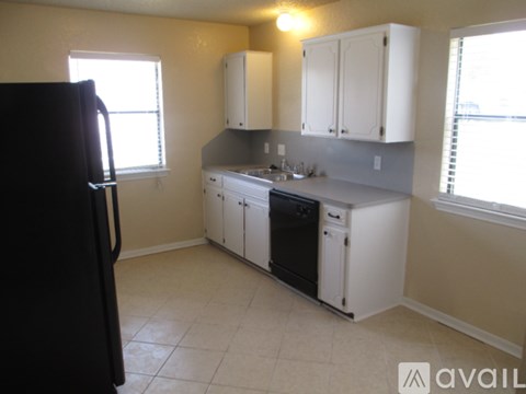 A kitchen with white cabinets and a black refrigerator.
