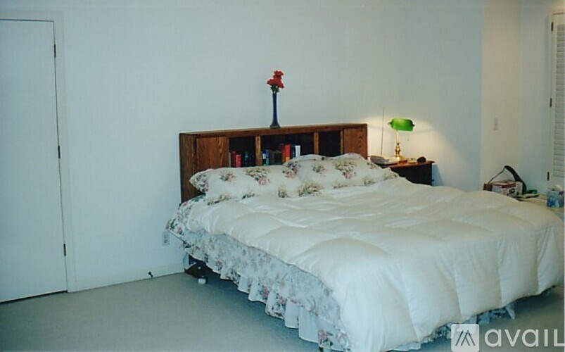 A bed with a white comforter and a red flower on the headboard.