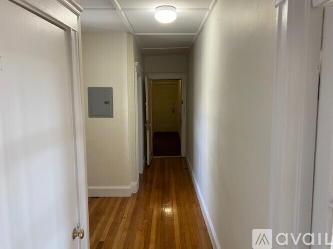 A long hallway with a door at the end and a light switch on the wall.