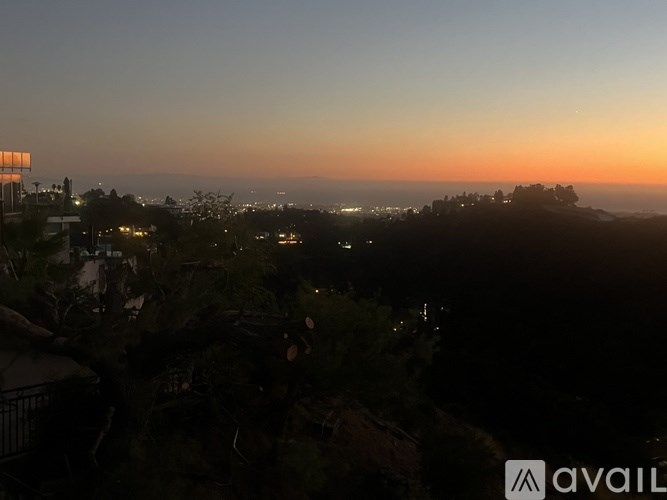 A sunset view from a hilltop with a building and trees in the foreground.