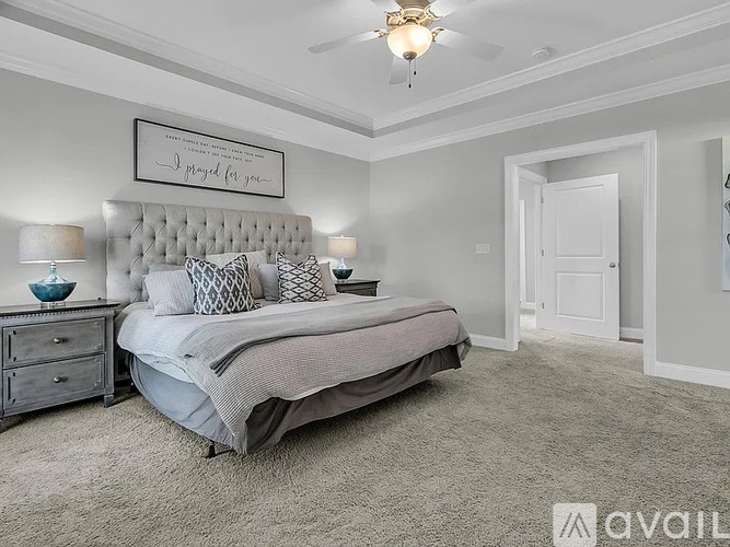 A bedroom with a large bed, a nightstand with a lamp, and a framed sign on the wall.