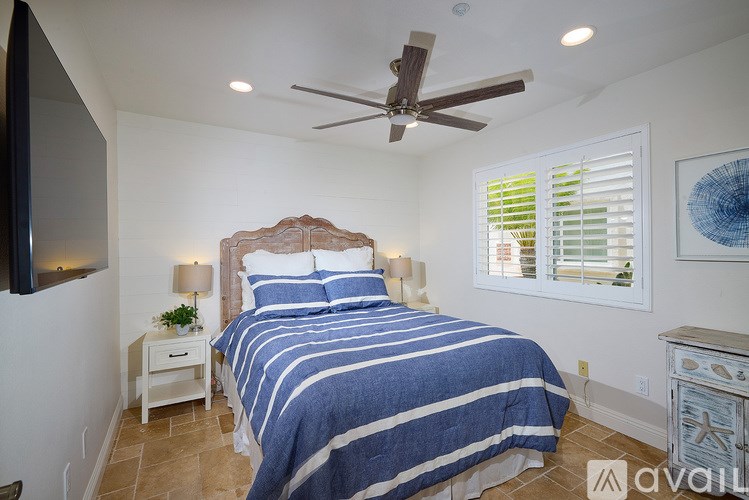 A bedroom with a bed, a ceiling fan, and a nightstand with a plant on it.