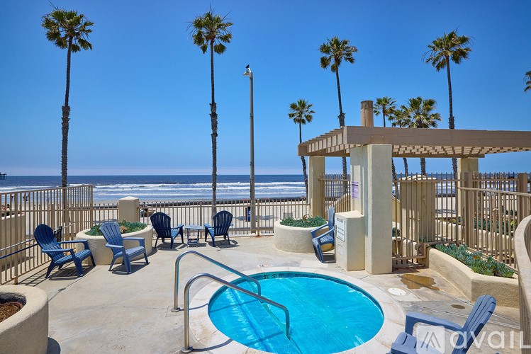 A pool area with a hot tub, chairs, and palm trees.