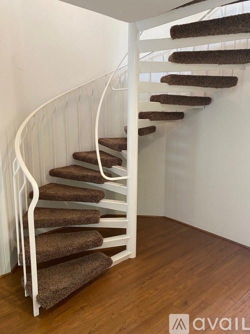 A spiral staircase with brown carpeted steps and white railings.