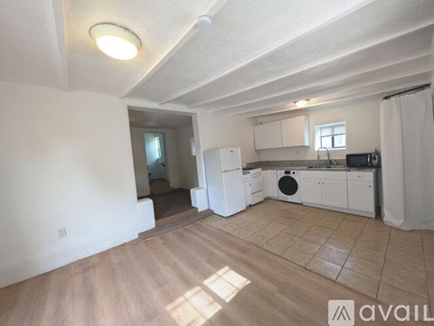 A kitchen area with white cabinets and appliances, and a wooden floor.