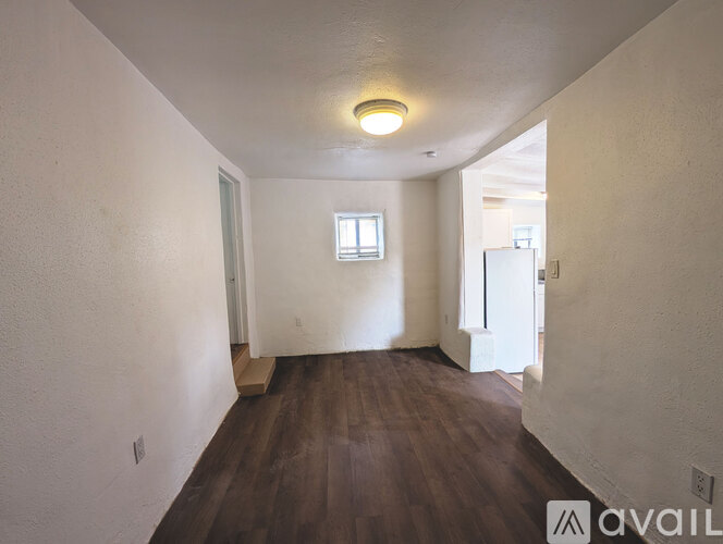 A room with wooden floors and white walls, with a window and a door visible.